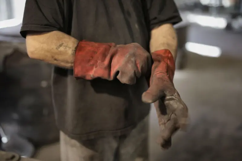 Trabajador ajustándose guantes de cuero de uso rudo en un taller