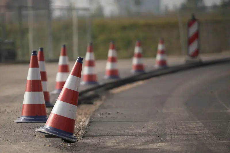 Fila de conos de seguridad naranjas con franjas blancas delimitando el borde de una vía en obra