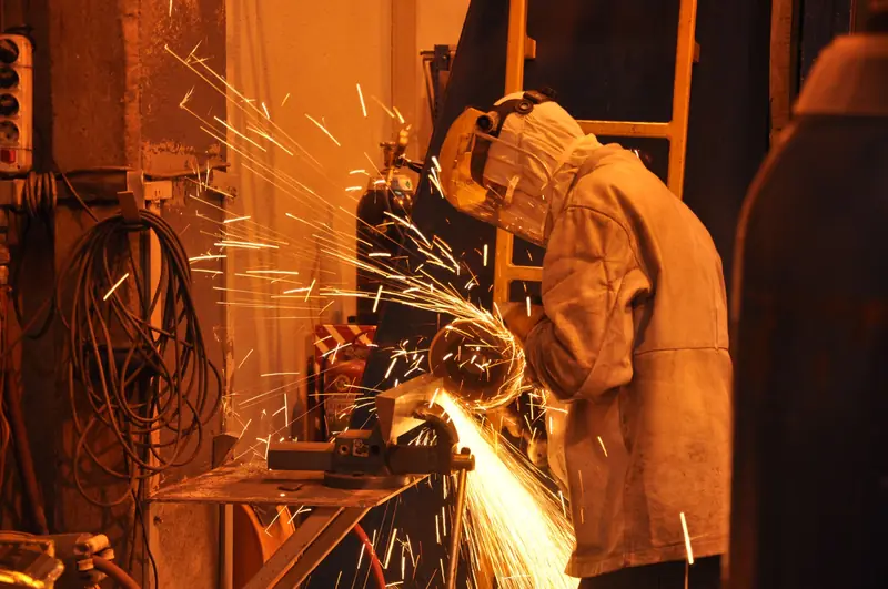 Trabajador con careta facial y casaca de cuero cortando metal con amoladora entre chispas