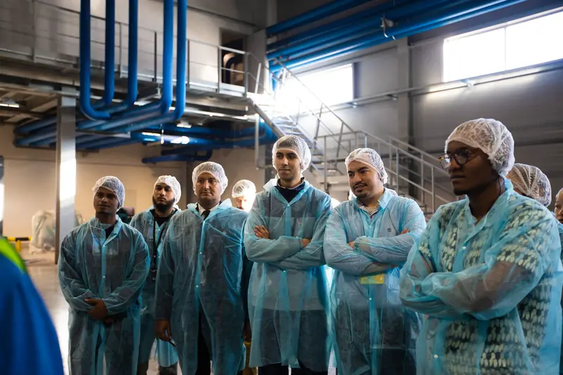Grupo de trabajadores con batas descartables y cofias escuchando una inducción dentro de una planta industrial