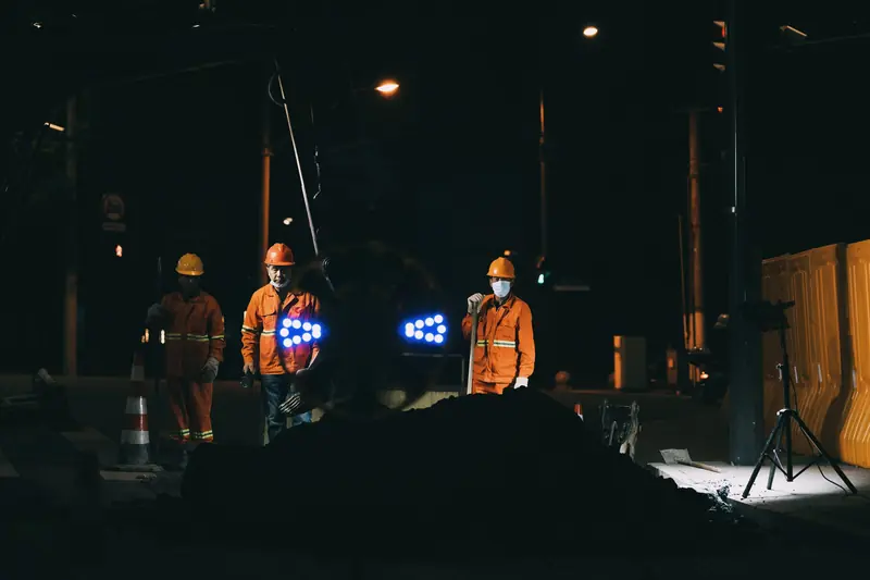 Cuadrilla nocturna en una vía con cascos, mascarillas y ropa reflectiva naranja junto a conos y luces de obra
