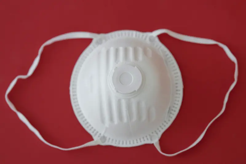 Respirador descartable blanco tipo N95 con válvula sobre fondo rojo, sin marcas visibles
