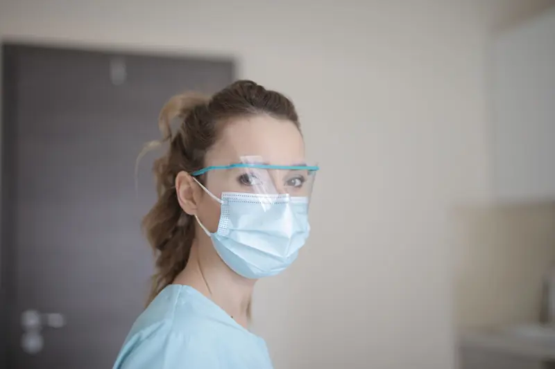 Profesional de salud con uniforme celeste, mascarilla y lentes protectores en un pasillo clínico