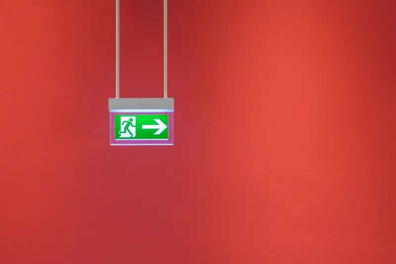 Señal luminosa verde de salida de emergencia con pictograma y flecha, sin texto, sobre una pared roja
