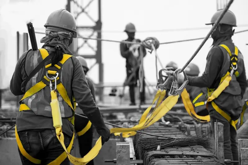 Trabajadores con arneses de cuerpo completo amarillos y líneas de vida en una obra, en blanco y negro con los arneses en color