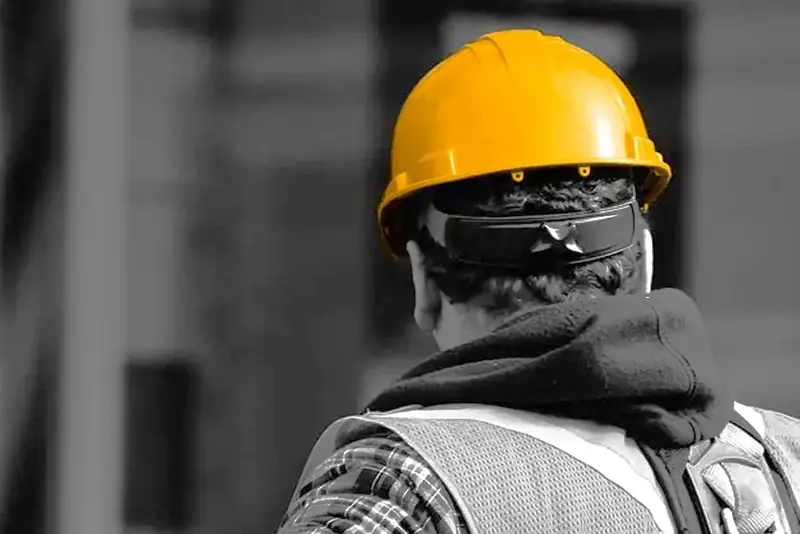 Trabajador visto de espaldas con casco de seguridad amarillo, en una foto en blanco y negro donde solo el casco conserva el color